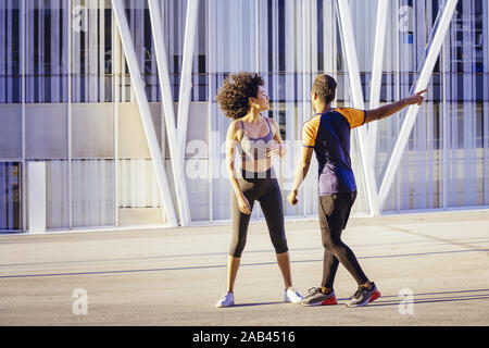 athletic latin woman and sporty black man getting ready to run together in the city street with a building in the background. urban sports workout in Stock Photo