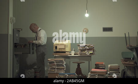 Corporate businessman searching for files in a rundown messy office with outdated computer and piles of paperwork Stock Photo