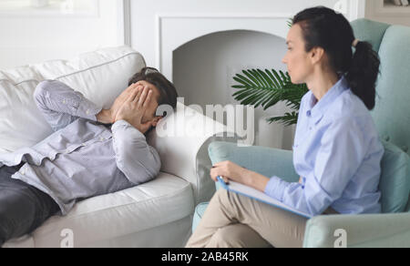Crying deeply depressed man laying on coach at therapist office Stock Photo