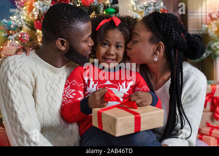 Afro parents kissing their daughter in cheeks while giving Christmas present Stock Photo