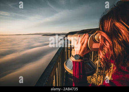 woman sitting on mountain peak watching sunrise over a sea of fog Stock Photo