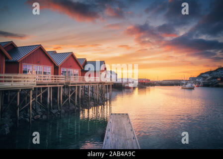 Red rorbu on wooden piles on sea coast, small jetty, colorful sky Stock Photo