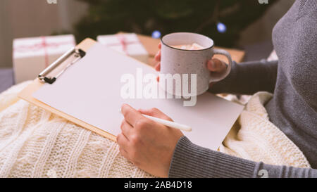Female writing her Christmas wishes on white clipboard Stock Photo