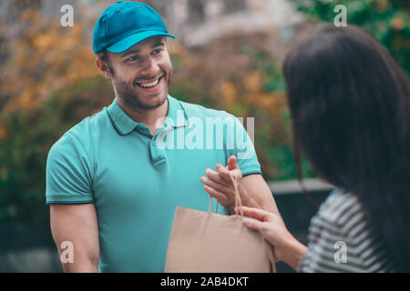 Cheerful bearded delivery man smiling while talking to woman Stock Photo