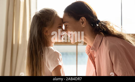 Cheerful mother and cute daughter touching noses in sunny room Stock Photo