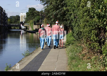 a group of people walking away from camera along a towpath all dressed in red striped t shirts and hats and wearing blue jeans Stock Photo