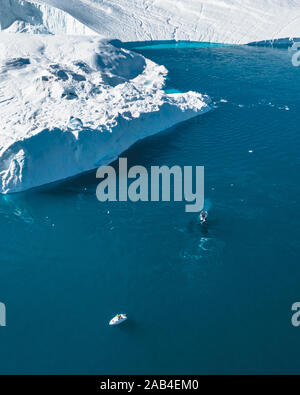Humpback whale diving near small fishing boat ship, boat, showing on the dive. Icebergs with blue ocean water. Greenland Disko Bay area near ilulissat Stock Photo