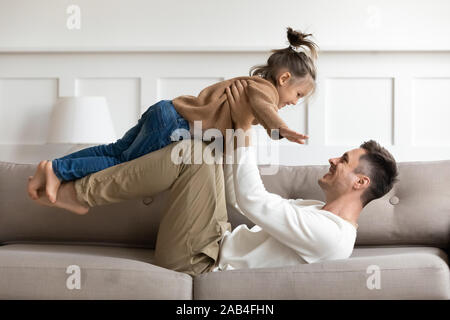 Happy father lifting cute kid daughter up playing on sofa Stock Photo