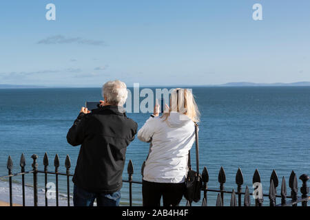 Senior / middle-age couple on holiday at seaside taking pictures of view on mobile phones Stock Photo