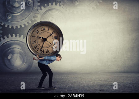 Bent down guy carrying a big heavy clock on his back. Overloaded student tired of daily tasks, and difficult burden. Time pressure and management conc Stock Photo