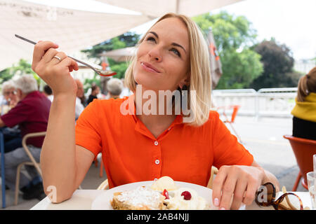 Young woman sits in a cafe in Vienna and eats Austria's traditional sweet apple strudel with whipped cream and vanilla ice cream, Vienna, Austria Stock Photo