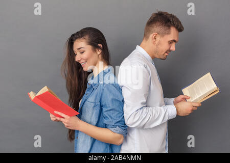 Relationship Concept. Young couple studio standing back to back isolated on grey reading books joyful Stock Photo