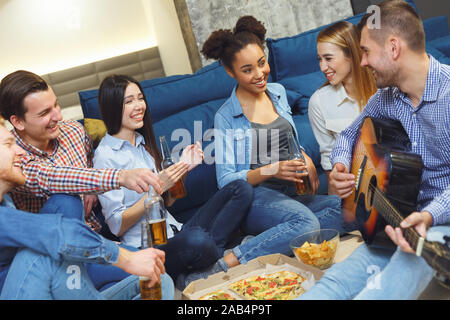 Group of friends having party indoors fun together guy playing guitar Stock Photo