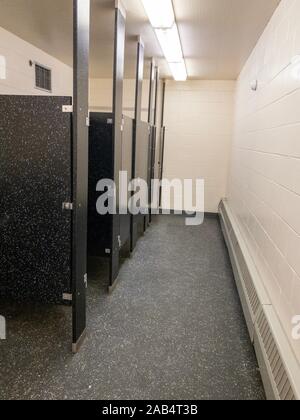 Inside a tiled public restroom with cubicle doors opening to the left illuminated by neon lights in a receding view Stock Photo