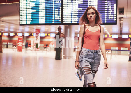 Beautiful young tourist girl with backpack in international airport, near flight information board Stock Photo