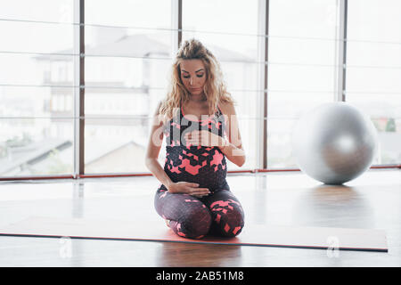 Concept of Yoga and Fitness Pregnancy. Portrait of a young model of a pregnant woman developing indoors. Stock Photo