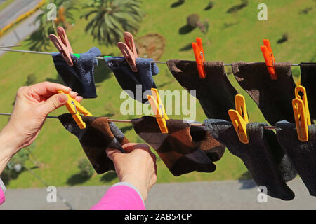 Closeup woman's hand hanging socks on clothesline with clothespin on the upper floor Stock Photo