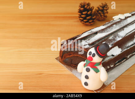 Closeup a Cute Snowman Marzipan of Christmas Roll Cake on Wooden Table with Blurry Dry Pine Cones in Background Stock Photo