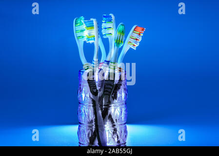 Many new plastic toothbrushes inside a glass, isolated on striking blue background, with copy space. Stock Photo