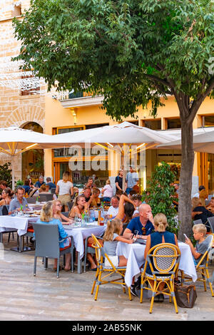 ALCUDIA, SPAIN - July 8, 2019: Restaurant tables on street with tourists in seaside Alcudia old town, Mallorca island, Spain Stock Photo