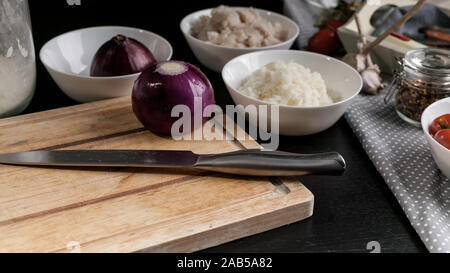 Chef's knife, red onions, cod fish meat, rice, cherry tomatoes and olives. Ingredients for homemade fish pie. Kitchen still life Stock Photo