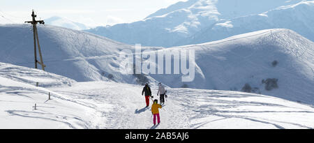 Skiers and snowboarders on snow road at sun winter morning. Caucasus Mountains, Georgia, region Gudauri. Panoramic view. Stock Photo