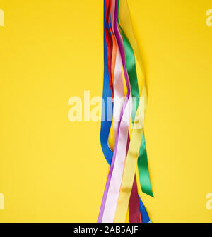 many silk multi-colored ribbons on a yellow background, top view Stock Photo