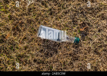 An empty discarded miniature glass liquor bottle laying on the grass outdoors thrown to the ground as garbage on a sunny day in autumn Stock Photo