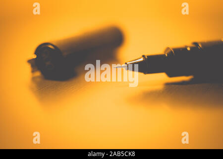 Black pen on a orange notebook paper, accessory for creativity on the table. Stock Photo