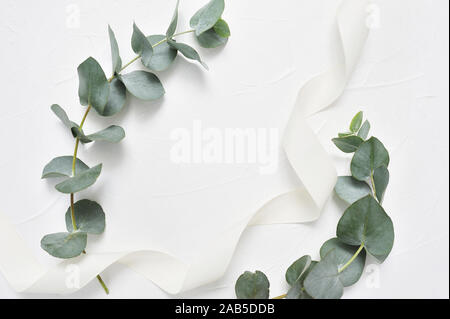 Eucalyptus leaves and ribbon frame on white background. Wreath made of leaf branches. Flat lay, top view with place for your text Stock Photo