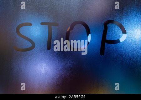 the word stop written on night wet window glass close-up with blurred background. Stock Photo