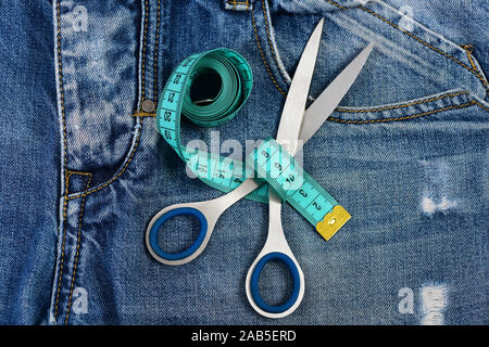 Making clothes and design concept. Tailors tools on denim fabric, selective focus. Jeans crotch and pocket, close up. Measure tape wound around metal scissors on jeans. Stock Photo