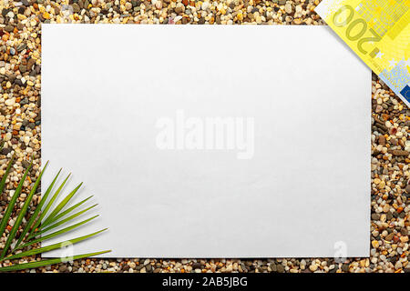 White sheet of paper for text with fern and euro lie on the sea sand. Stock Photo