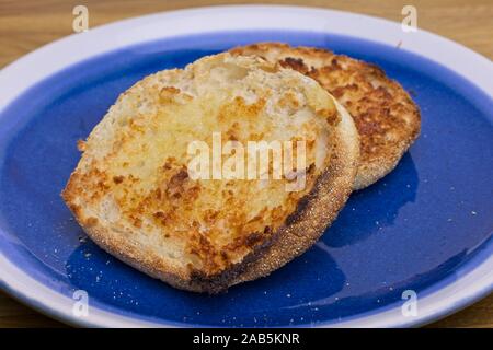 Hot toasted muffins cut in half and buttered on a blue plate. Stock Photo