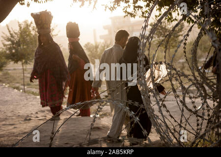 Kuchi nomad women walk by on the other side of coils of barbed wire laid along a frquently used path in Kabul, Afghanistan Stock Photo