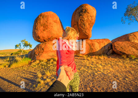 Hand in hand couple at Devils Marbles, Northern Territory: the Eggs of mythical Rainbow Serpent. Follow me, tourist woman at iconic landscape of Stock Photo