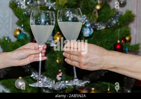 glasses with sparkling wine in male and female hands against the background of the Christmas tree, close-up Stock Photo