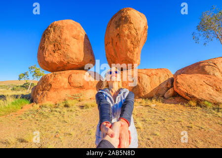 Couple hand in hand at iconic Devils Marbles in Northern Territory: the Eggs of mythical Rainbow Serpent. Follow me, tourist woman at Outback Stock Photo