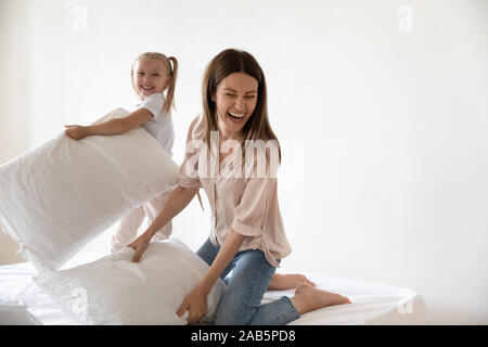 Carefree mom enjoying fighting pillows with small daughter on bed Stock Photo