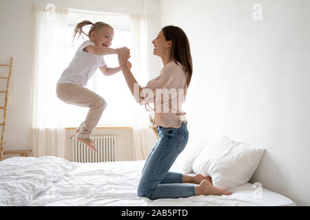 Cheerful mum play with active kid girl jump on bed Stock Photo