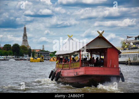 Bangkok, Thailand .11.24.2019: A red wooden traditional boat with tourist is crossing the Chao Phraya River towards the famous and amazing Wat Arun an