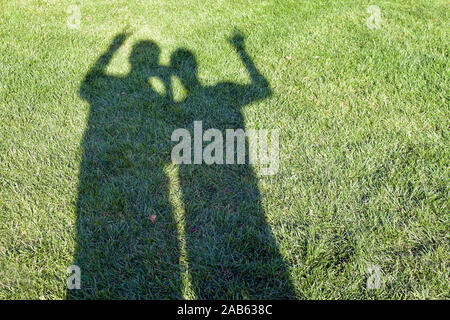 Against the background of green grass, two shadows of a man and a woman. Silhouettes of people on the lawn on a sunny summer day. Stock Photo