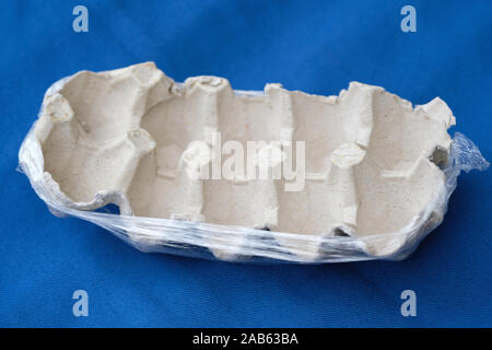 Empty egg tray close up. Cardboard egg tray in cellophane on a blue background. Disposable used paper egg container. Stock Photo