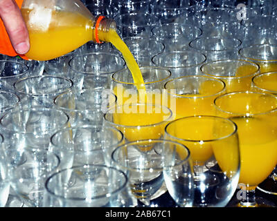 A yellow soft drink from a transparent bottle is poured into glasses standing ready and close to each other. Focus on the beam of the beverage Stock Photo