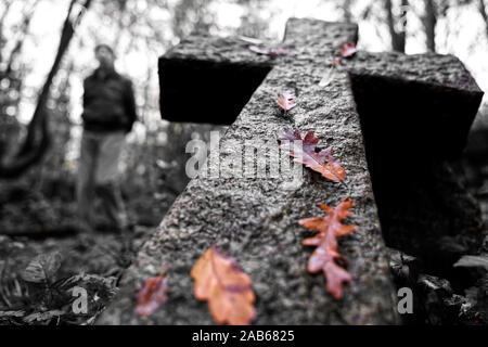 R.I.P. a stone cross falling down in a cemetery with a blurry man at one side and brown leaves on top Stock Photo