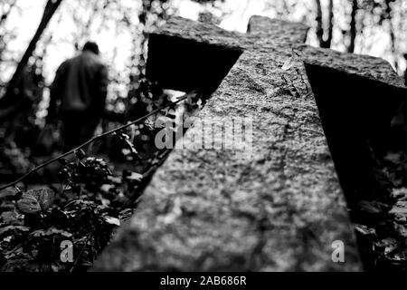 R.I.P. a stone cross falling down in a cemetery with a blurry man at one side Stock Photo