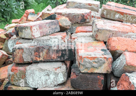 Many old used broken dirty burnt bricks with remnants of cement are stacked in rows on the grass in garden. Stock Photo