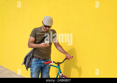 Trendy man using his smartphone outdoors while sitting on a fixed bike Stock Photo