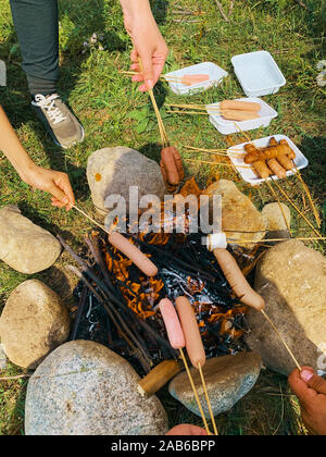 Campsite with friend. Cooking fried sausages and marshmallow on a fire in the forest. Stock Photo