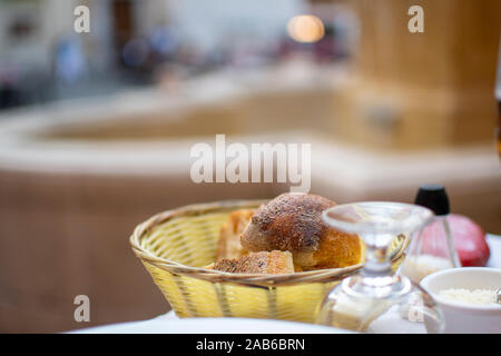 A basket of bread and rolls on a patio table in a piazza in front of a fountain in Nice France. Stock Photo